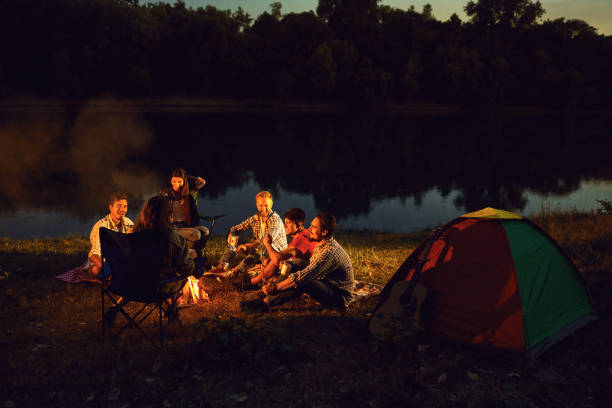 gli amici ridono seduti accanto al fuoco vicino alla tenda. - friendship camping night campfire foto e immagini stock