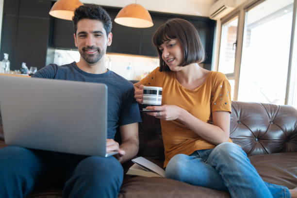 istock Couple using laptop while sitting on couch at home. 1320947610