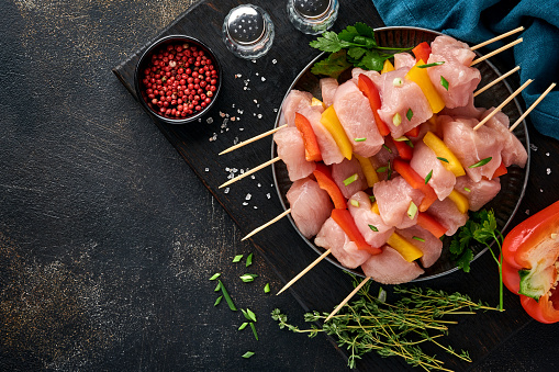 Raw shish kebab on wooden board, spices, herbs and vegetables on dark grey background. Barbecue Raw ingredients for goulash or shish kebab. Top view. Free copy space.