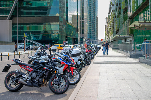 Moscow. Russia. May 26, 2021. Many motorcycles are parked against the backdrop of the skyscrapers of the Moscow City business center. Warm sunny day. Pedestrians walk along the sidewalk.