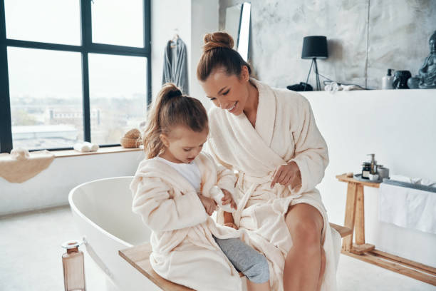 istock Mother with daughter in bathrobes smiling and using hand cream 1320950623