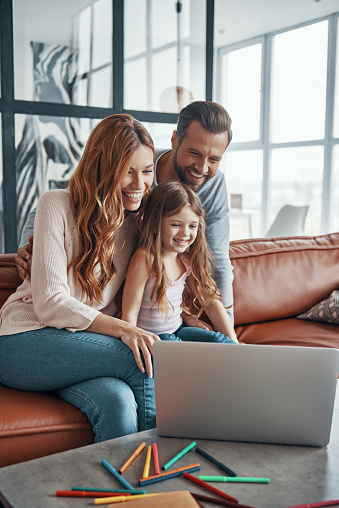 Young beautiful family with little girl bonding together and smiling while using laptop at home