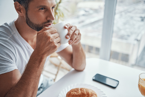 Top view of relaxed young man enjoying hot coffee while sitting at the kitchen