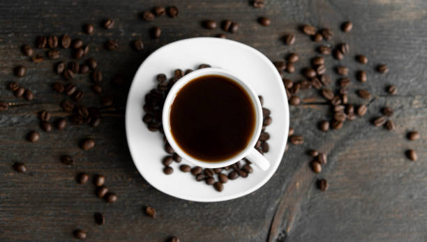 木製のテーブルの背景に焙煎コーヒー豆とコーヒーカップ。木製のテーブルの上に散らばったコーヒー豆と黒いコーヒーのマグカップ。新鮮なコーヒー豆。 - コーヒー　淹れる ストックフォトと画像