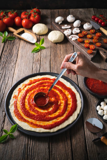 italian pizza male hand ladle spreading tomato sauce on pizza dough with ingredients mozzarella - mozzarella cheese italy tomato imagens e fotografias de stock