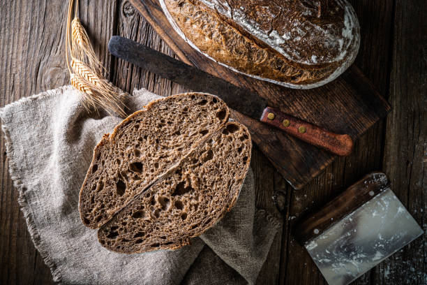 закваска хлеб хлеб и корзина banneton в пекарне на деревянном деревенском столе - brown bread bread home interior food стоковые фото и изображения