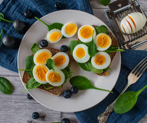 open faced sandwich with boiled eggs and spinach leave served with blueberries on a plate
