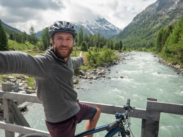 istock Young man mountain biker on bridge takes selfie 1320953828