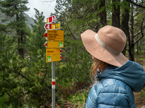 View of woman hiking on mountain trail looking at signs, Switzerland
