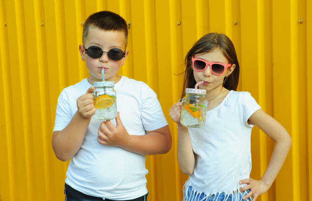 little friends in white t-shirts hold summer cold cocktails with orange and mint on a yellow background - drinking little girls women wine imagens e fotografias de stock