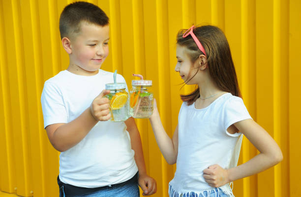 little friends in white t-shirts hold summer cold cocktails with orange and mint on a yellow background - drinking little girls women wine imagens e fotografias de stock