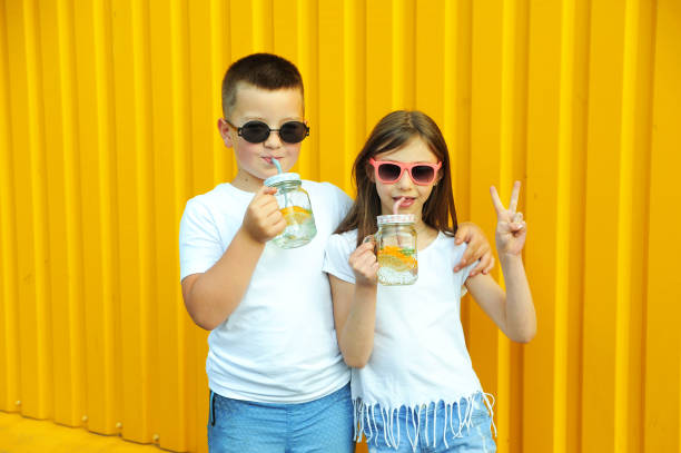 маленькие друзья в белых футболках держат летние холодные коктейли с апельсином и мятой на желтом фоне - drinking little girls women wine стоковые фото и изображения