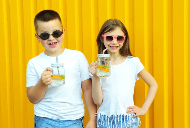 little friends in white t-shirts hold summer cold cocktails with orange and mint on a yellow background - drinking little girls women wine imagens e fotografias de stock