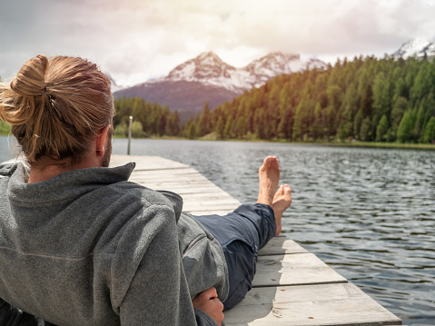 One person on wooden lake pier relaxing and enjoying mountain lake scenery