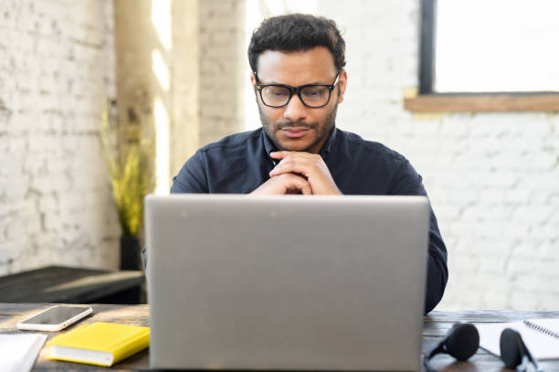 istock Thoughtful hindu freelancer guy wearing eyeglasses staring at the laptop screen 1320959250