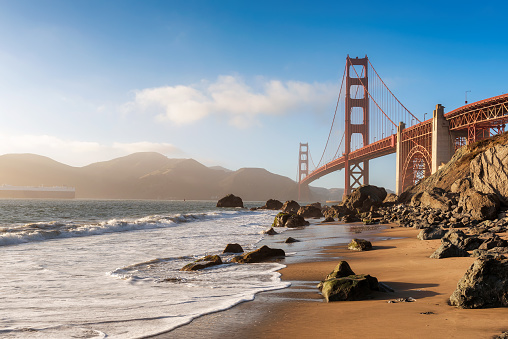 Golden Gate Bridge view from California beach, ocean wave, sand and rocks in Marshall’s Beach, San Francisco, California, USA