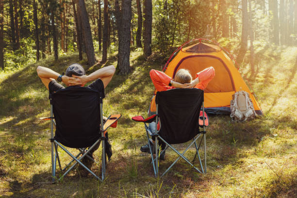 menschen, die sich auf campingstühlen auf dem waldcampingplatz entspannen und die natur genießen - campingstuhl stock-fotos und bilder