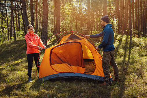 young couple set up a tent together in forest. outdoor adventure, camping trip