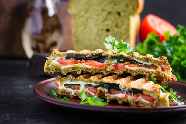 istock Vegetarian sandwich panini with spinach leaves, tomatoes and cheese on a dark table. Toast with cheese. 1320965562