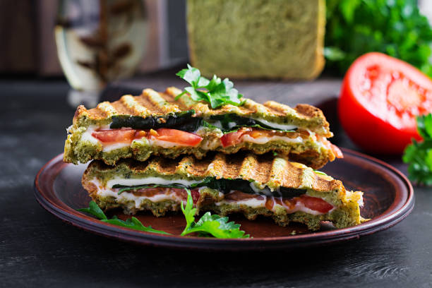 istock Vegetarian sandwich panini with spinach leaves, tomatoes and cheese on a dark table. Toast with cheese. 1320965569