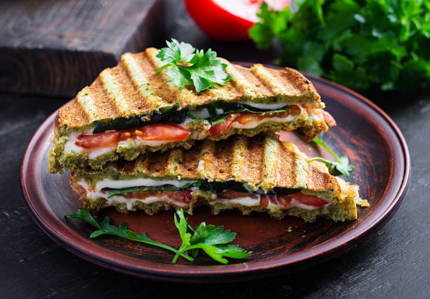 istock Vegetarian sandwich panini with spinach leaves, tomatoes and cheese on a dark table. Toast with cheese. 1320965570