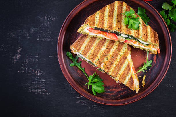 istock Vegetarian sandwich panini with spinach leaves, tomatoes and cheese on a dark table. Toast with cheese. Top view, overhead, copy space 1320965582