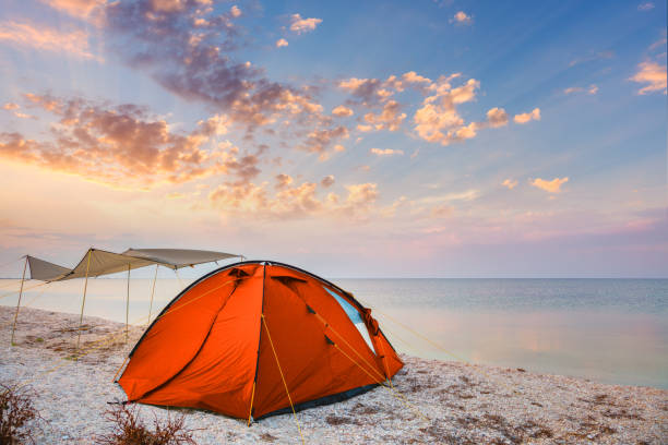 Camping tent on a beautiful quiet beach near the water against  the sunset sky background, happy summer time stock photo