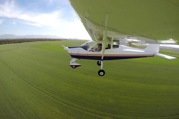 piloto en un avión sobrevolando campos verdes - avión ultraligero fotografías e imágenes de stock