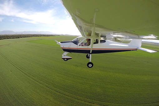 PILOT WITH A HIGH-WING SINGLE-ENGINE AIRCRAFT FLYING OVER GREEN CEREAL FIELDS IN SPRING