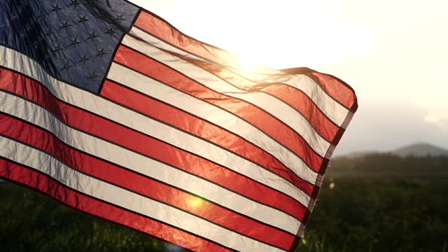 Close-up American flag waving over sunset in nature background, soft focus, Slow Motion. Concept of Memorial Day, 4th of July, Independence Day, Veterans Day, Celebrate USA, United States of American.