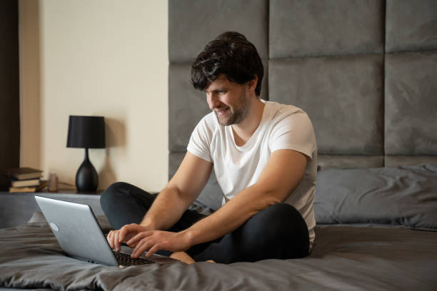 istock Excited man sitting on a bed with a laptop is celebrating success 1320968661
