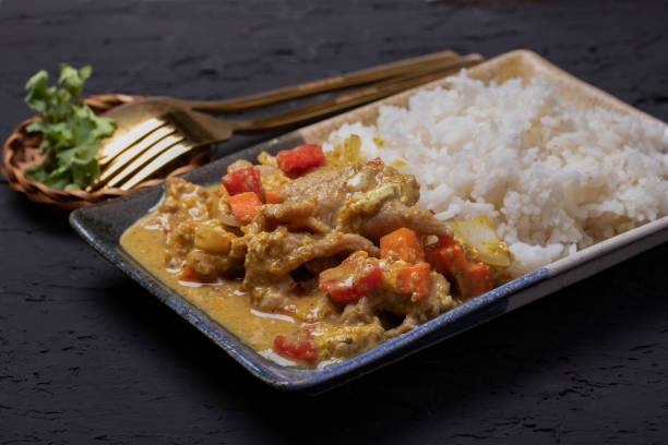 istock Stir fried pork curry powder with steamed rice in a plate on a black background. 1320969435