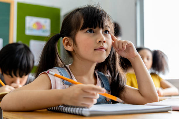 retrato de una niña asiática estudiante pensando y resolviendo el tema estudiado en el aula. concepto de educación escolar - niño de primaria fotografías e imágenes de stock