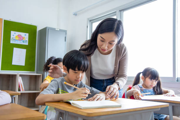 the girl and boy student take note lecture in the classroom. young woman teachers give advice on learning to diversity elementary school children. back to school concept - multi ethnic group concentration student asian ethnicity imagens e fotografias de stock