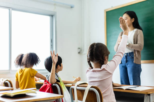 istock Diversity of elementary school students raise their hands to answer teacher questions in class room. Back to school concept 1320972259