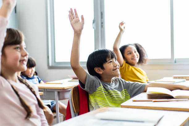 Diversity of elementary school students raise their hands to answer teacher questions. Back to school concept stock photo