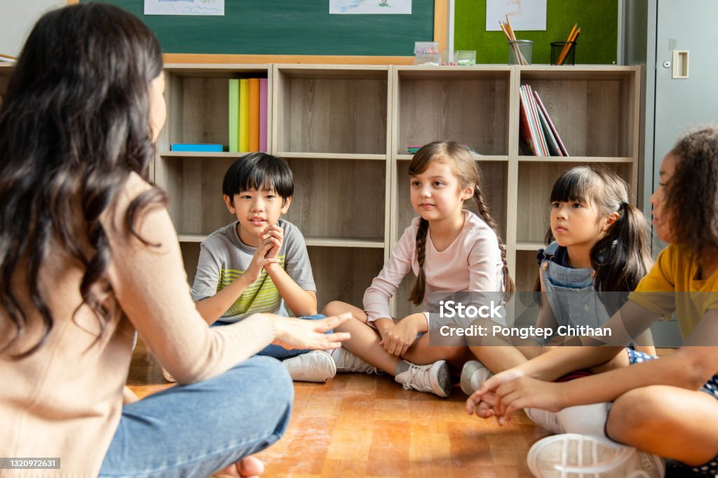 Diversity Elementary school students who sit on the classroom floor listen to Asian female teachers tell stories. Concept of education and learning Teacher Stock Photo