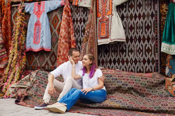 Photo of Couple in love buys a carpet and handmade textiles at an oriental market in Turkey. Hugs and cheerful happy faces of men and women