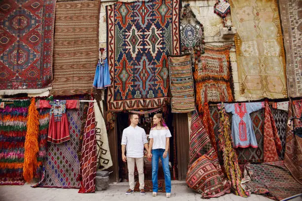 Photo of Couple in love buys a carpet and handmade textiles at an oriental market in Turkey. Hugs and cheerful happy faces of men and women