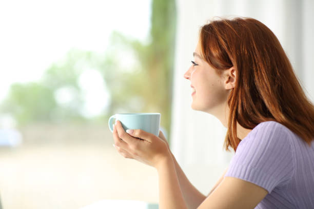 istock Happy woman drinking coffee looking through a window 1320974483