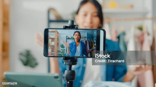 Young Asia Lady Fashion Designer Using Mobile Phone Receiving Purchase Order And Showing Clothes Recording Video Live Streaming Online At Shop Stock Photo - Download Image Now