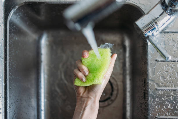 Close up photo of woman hand cleaning kitchen with a green sponge