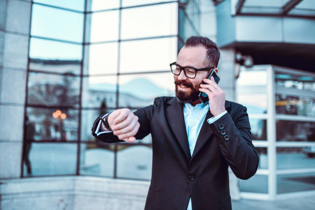 istock Modern Businessman Smiling And Looking At Time On Watch While Talking On Phone 1320984005