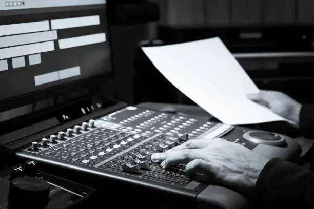 sound engineer hands adjusting volume on audio mixing board in broadcasting, post production studio