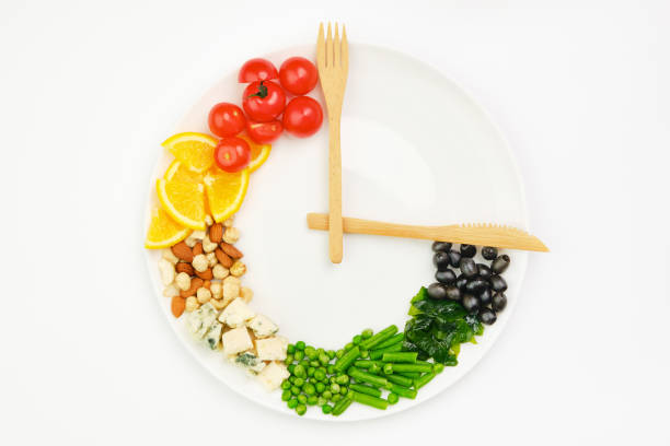 colorful food and cutlery arranged in the form of a clock on a plate. intermittent fasting, diet, weight loss, lunch time concept. - clock time alarm clock orange imagens e fotografias de stock