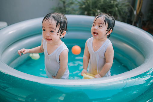 asian chinese twin babies playing in swimming pool during summer at backyard of house