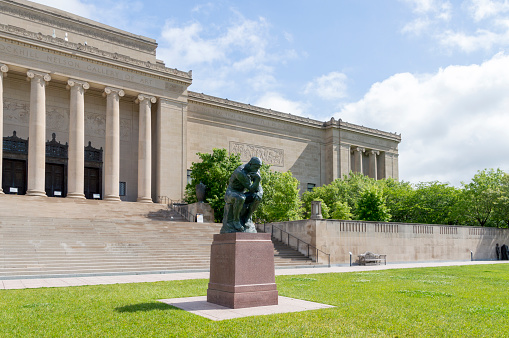 May 18, 2021 - Kansas City, Missouri, USA: This shot shows the stately entrance on the south side of the Nelson-Atkins Museum in Kansas City, Missouri including a larger Thinker sculpture.  This distinctive landmark is a centerpiece for the city.  This shot was taken on a rainy spring day with clouds in the background and the sun making a brief appearance.