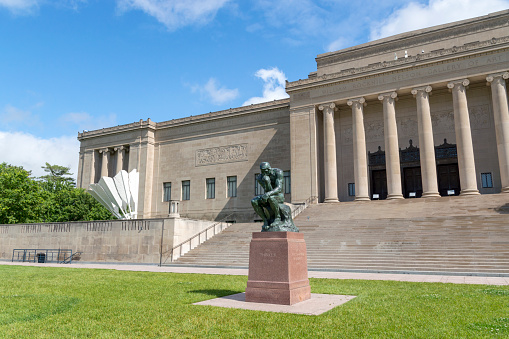 May 18, 2021 - Kansas City, Missouri, USA: This shot shows the stately entrance on the south side of the Nelson-Atkins Museum in Kansas City, Missouri including a large Thinker sculpture.  This distinctive landmark is a centerpiece for the city.  This shot was taken on a rainy spring day with clouds in the background and the sun making a brief appearance.
