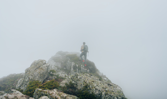 Photo of a young man on the mountain peak on a foggy day