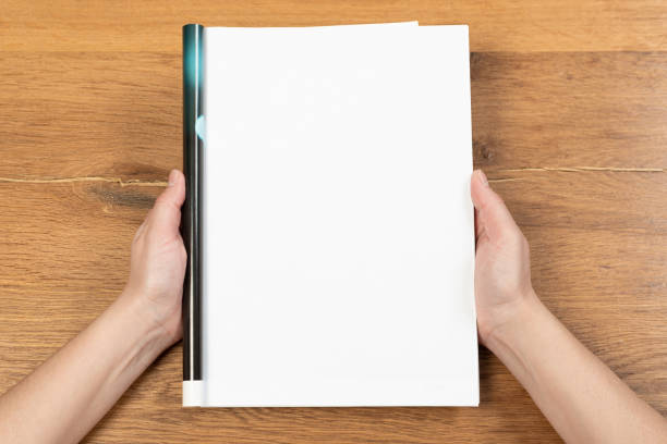 istock Woman's hands open empty catalog, magazines, book mockup on wooden table 1320992988